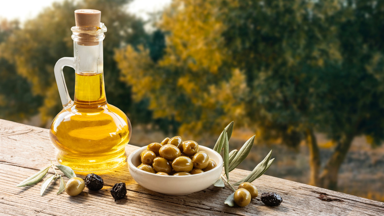 Jug of olive oil next to a bowl of olives on a wooden table