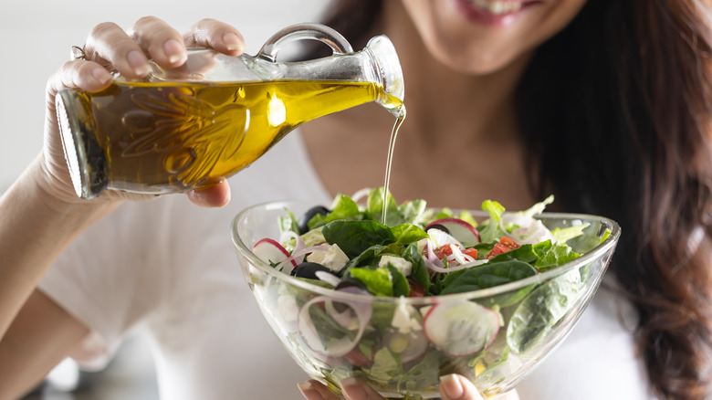 Person pouring olive oil on a salad