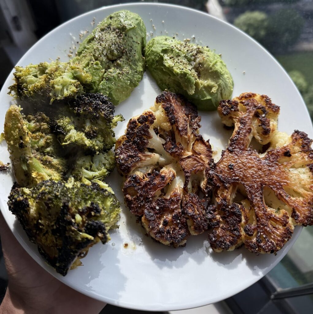 Grilled cauliflower steak accompanied by organic broccoli, creamy Haas avocado, and a side of roasted Brussels sprouts.