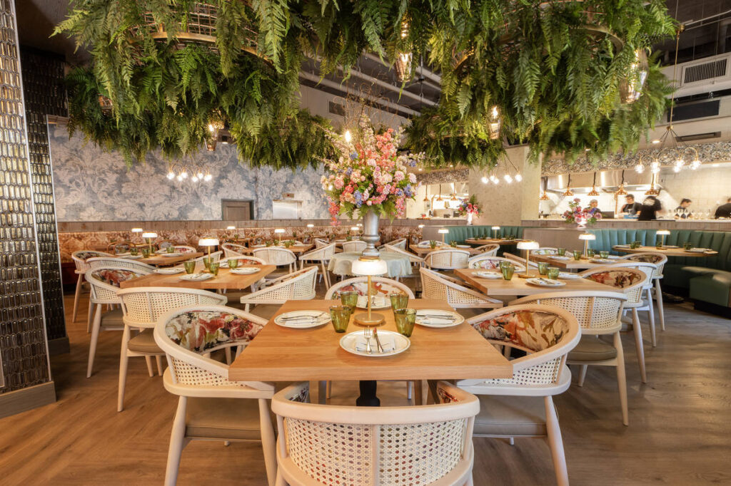 interior of La Serre with colorful decor, handmade antiqued brass chandeliers that are flush with living botanicals, Venetian plaster, English flower troughs, floral booths, and antique mosaic tiles reminiscent of the French Riviera