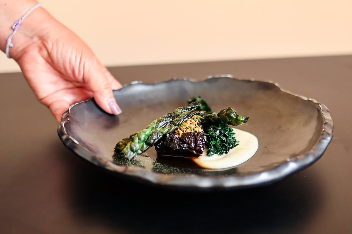 small portion of beef with vegetable garnishes on black plate