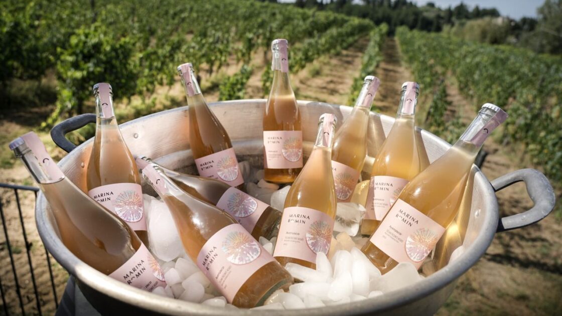 Image of a large metal tub full of Marina Romin pink dessert wine bottles and ice, set against a backdrop of the vineyards.