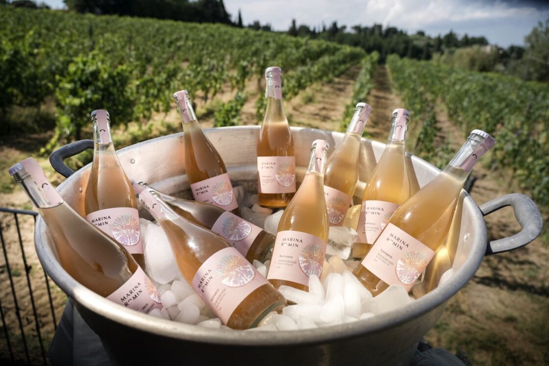 Image of a large metal tub full of Marina Romin pink dessert wine bottles and ice, set against a backdrop of the vineyards.