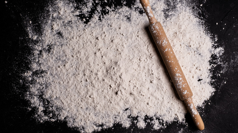White flour spread over a black surface with rolling pin