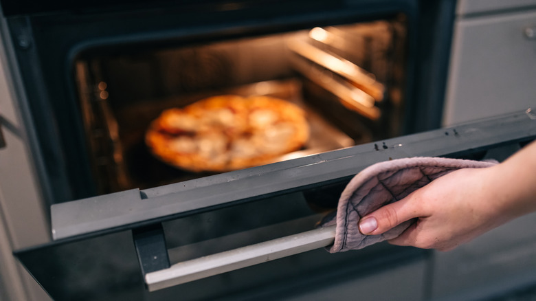Person opening oven with pizza inside