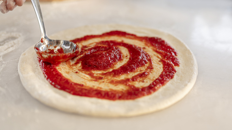 Pizza sauce being swirled over dough with bottom of spoon