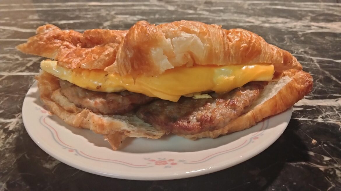 Sausage patty cut in half and assembled lengthwise, scrambled folded egg, and cheese, on a croissant