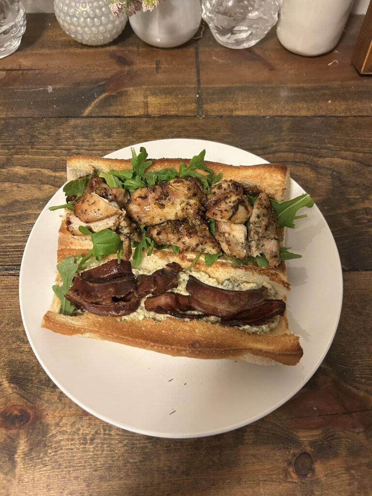 Chicken and bacon with homemade whipped burrata and pesto spread, jammy roasted balsamic garlic and cherry tomatoes, and arugula on a toasted French roll