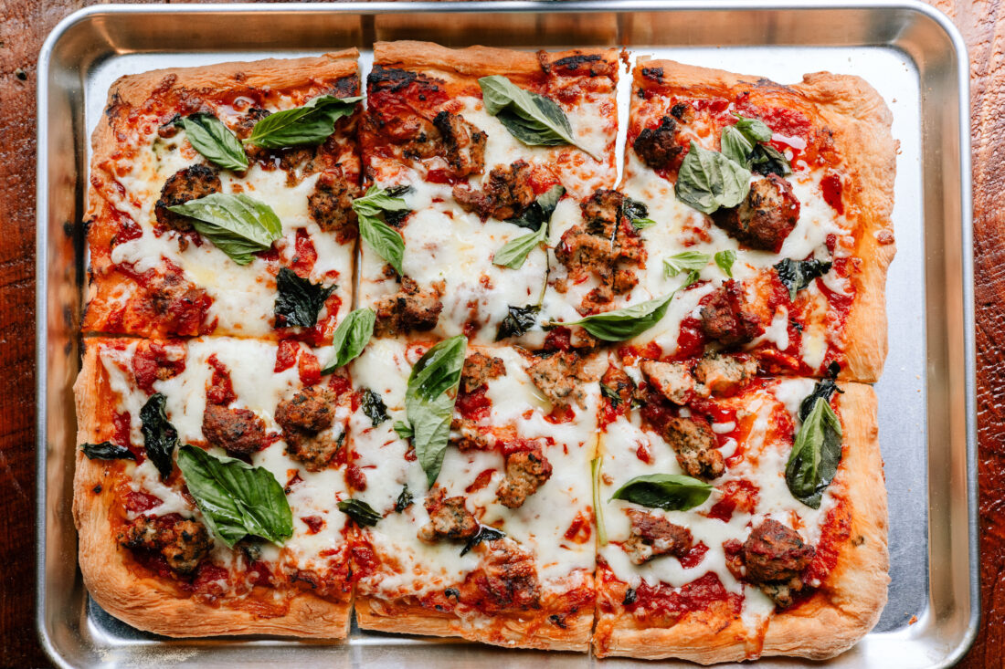 A square pizza with meat and basil