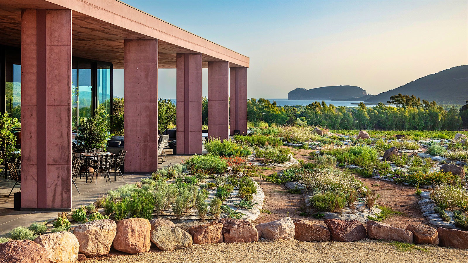 The wood-clad exterior of Guardia Grande winery with a view of the Sardinian landscape and the sea behind it