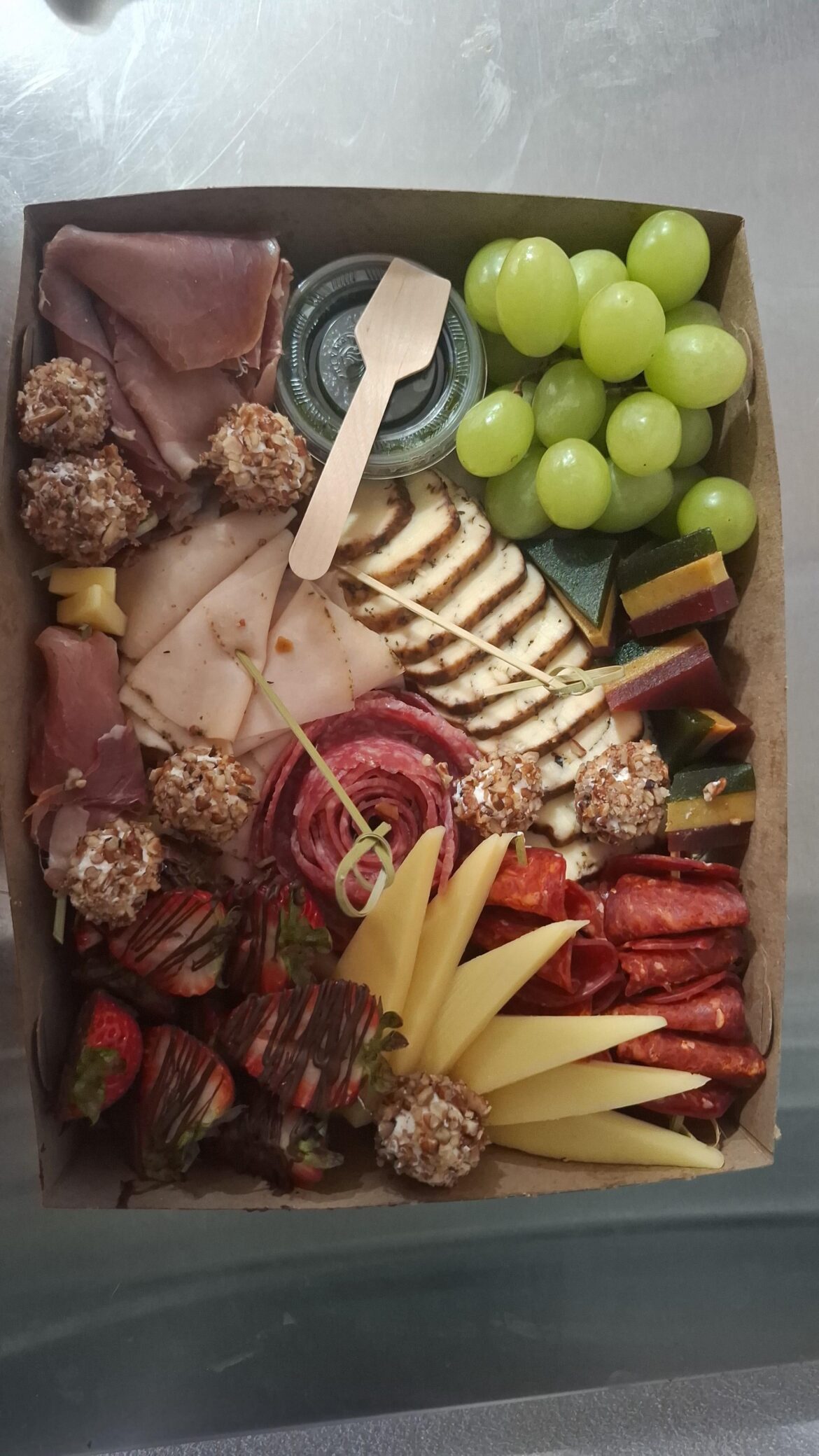 Charcuterie box for 2 people: provolone with fine herbs, salami, aged pepperoni, grapes, strawberries with chocolate, "ate" (mexican candy made from fruits), artisanal turkey breast ham with italian herbs, cream cheese balls with nuts and a pesto dip