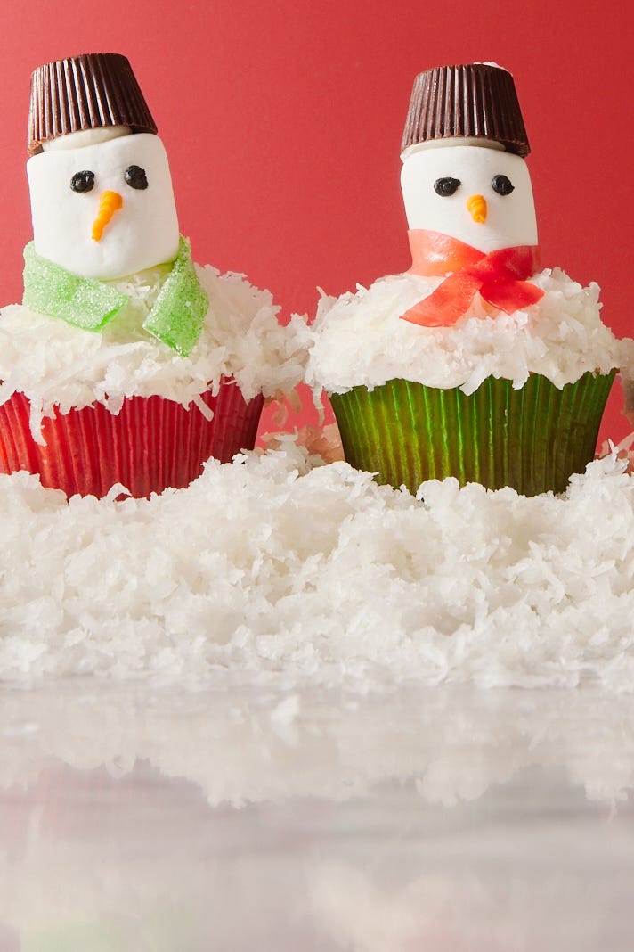 snowman cupcakes topped with shredded coconut snow, marshmallow faces, candy scarves, and peanut butter cup hats