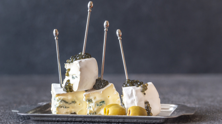 Chunks of soft cheese with veins of mold topped with caviar with green olives and silver picks