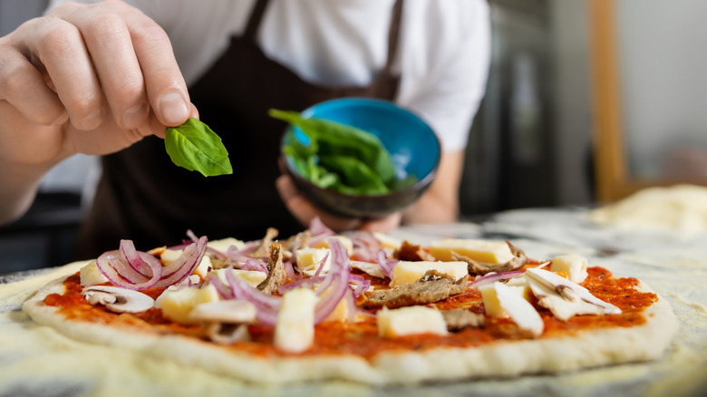 Person placing toppings on a pizza