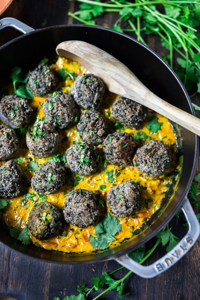 lentil meatballs in pan with creamy coconut curry sauce, topped with fresh herbs. 