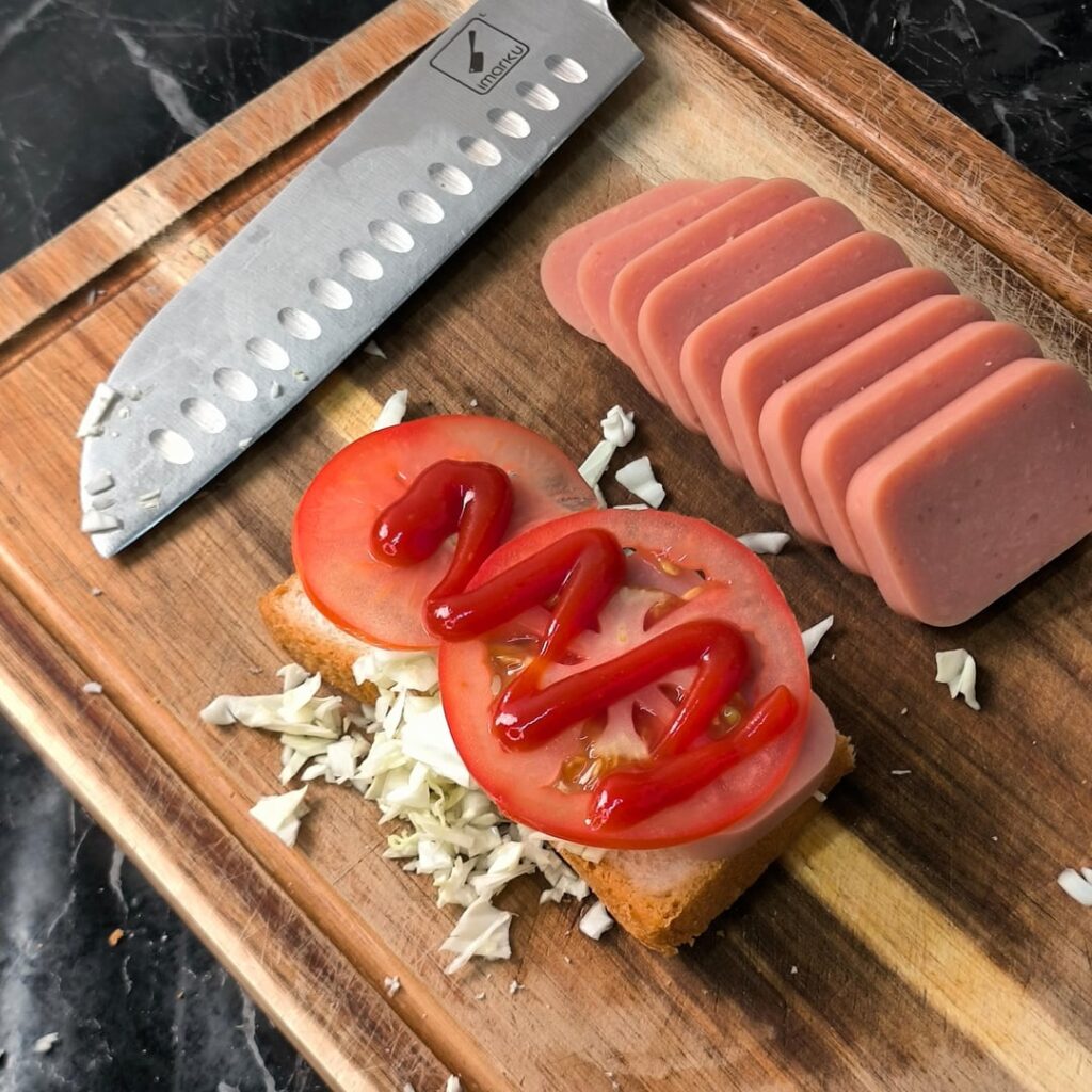 Sandwich with sliced tomato, shredded cabbage, ham, and salad dressing on white toast