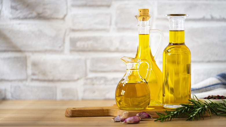 Glass bottles of cooking oil arranged on a wooden board near shallots and herbs.