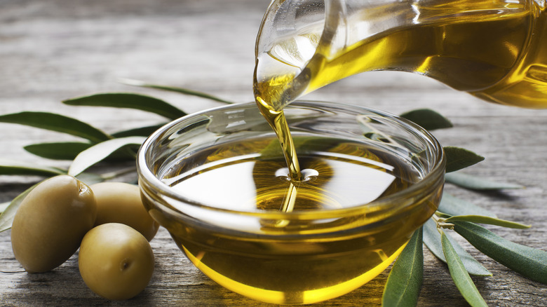 Golden olive oil being poured from a glass carafe into a small bowl