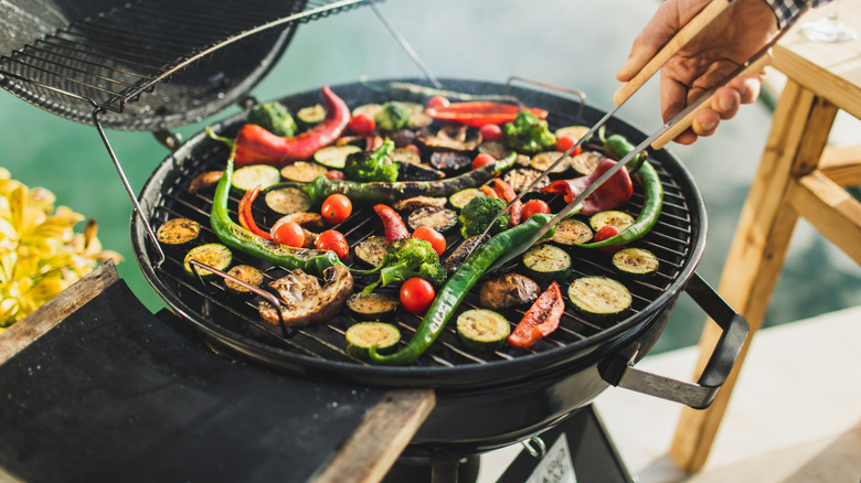 A person bbqing vegetables: zucchini, pepper and chile