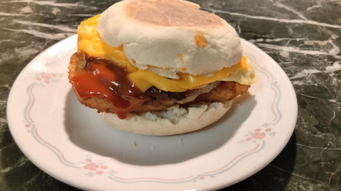 Hash brown patty, sausage patty, fried egg, and cheese with sriracha on an English muffin
