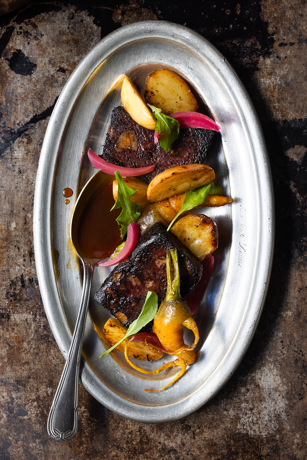 Overhead view of a plated dish featuring blood sausage, roasted potatoes, and vegetables.
