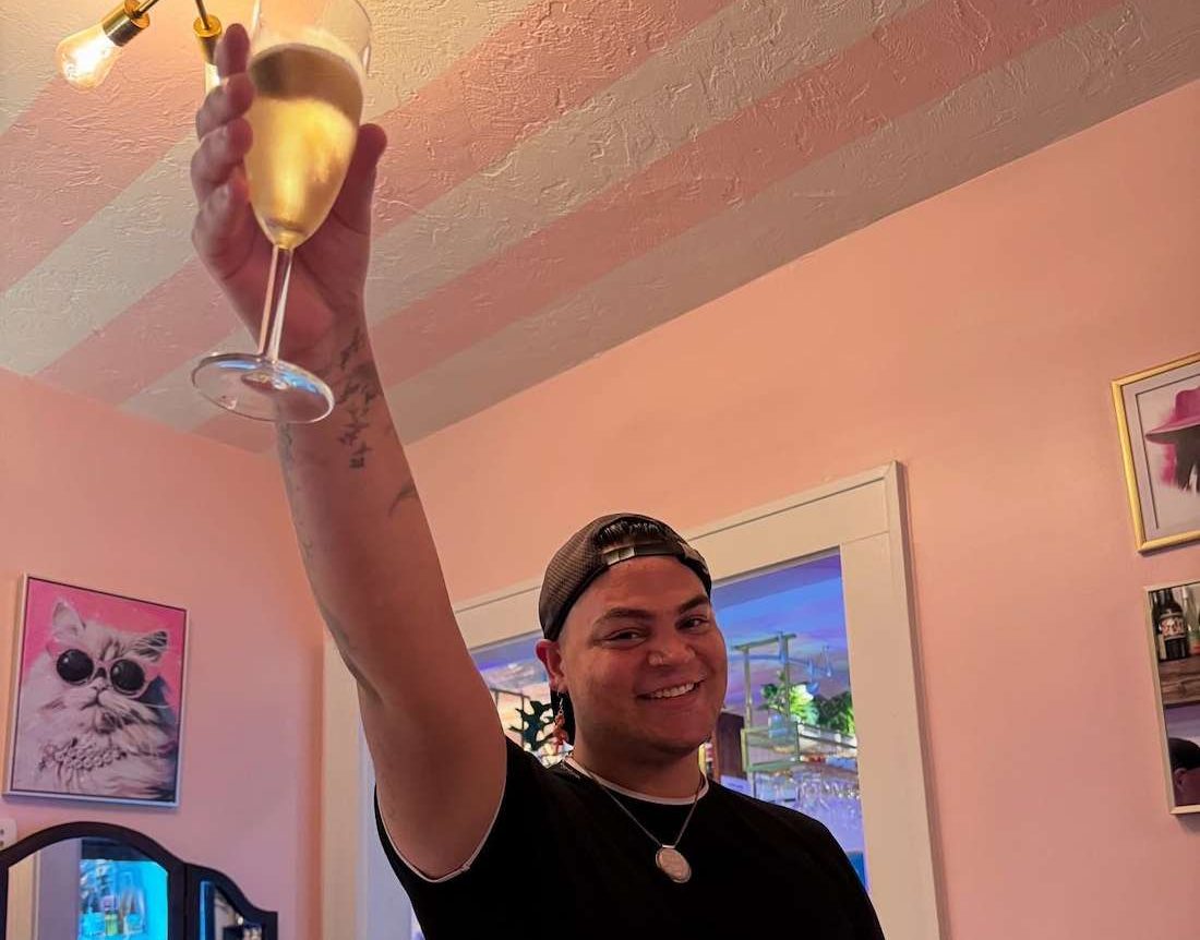 a man in a black t-shirt holding up a glass of wine while smiling.