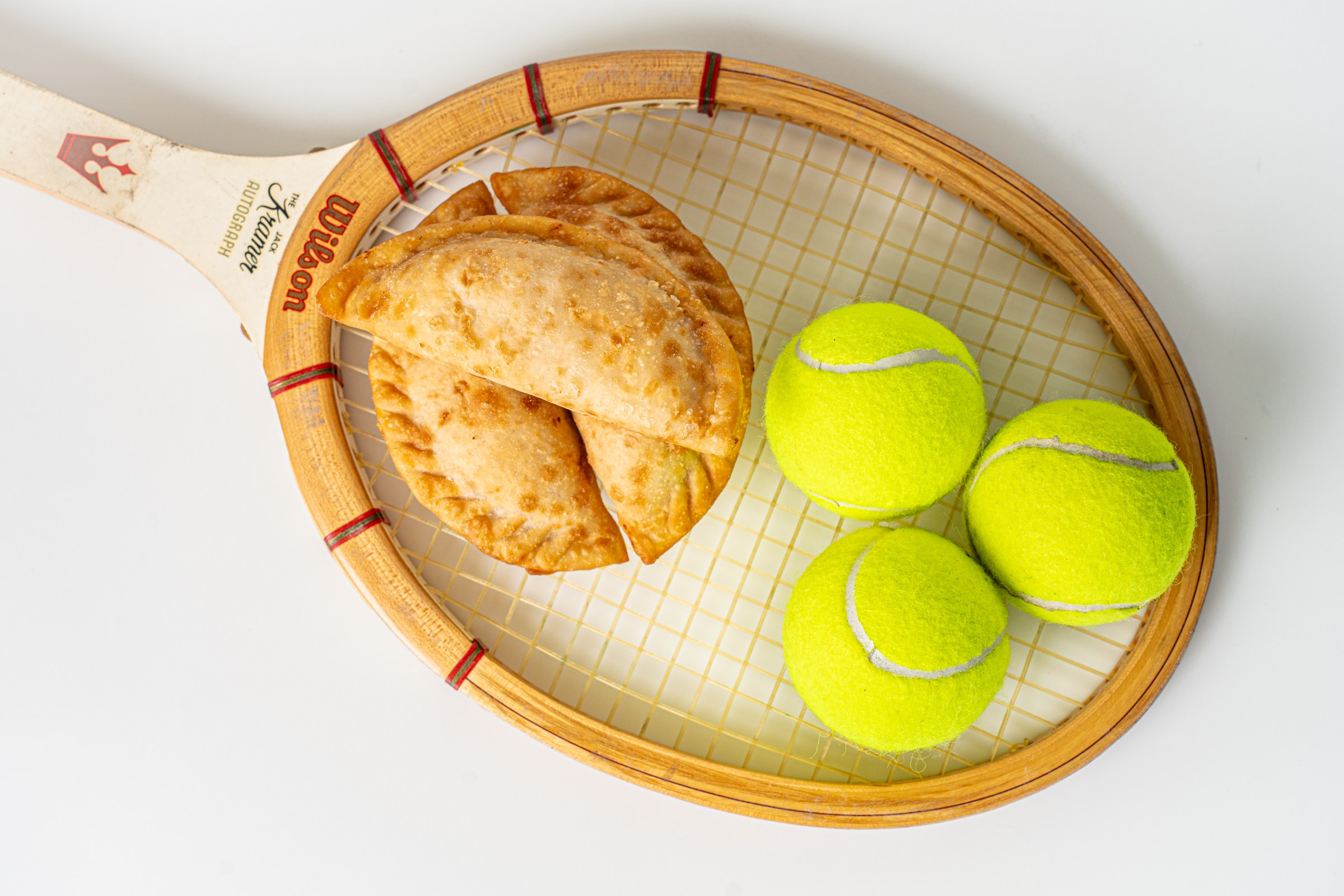 A tennis racquet with empanadas and tennis balls on it.