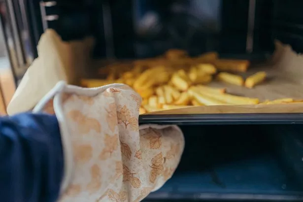Someone taking french fries from the oven.