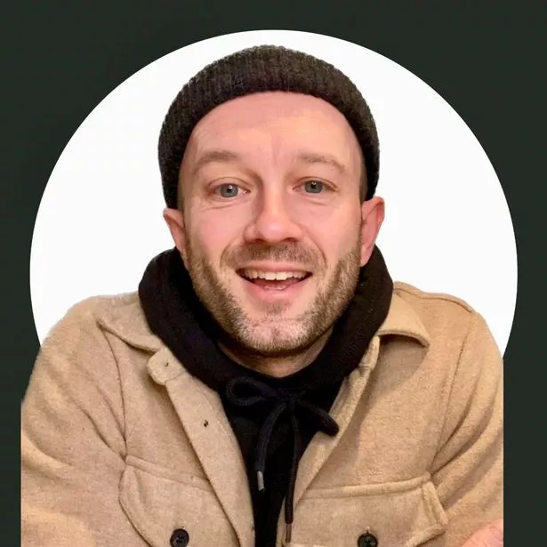 A picture of Liam D'Arcy smiling into the camera wearing a beanie hat, black hoodie and a beige corduroy jacket