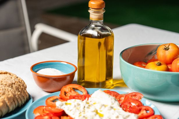 Setting a table outdoors with a fresh salad made with tomatoes, cheese and herbs, a loaf of bread, a bowl of tomatoes, salt and a bottle of olive oil