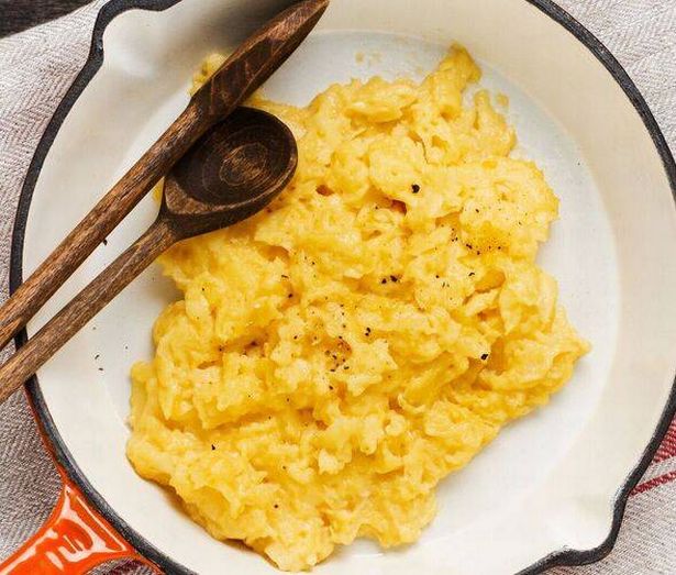 Scrambled eggs for breakfast on frying pan, dark wooden table background. Traditional English breakfast.Top view with cope space.