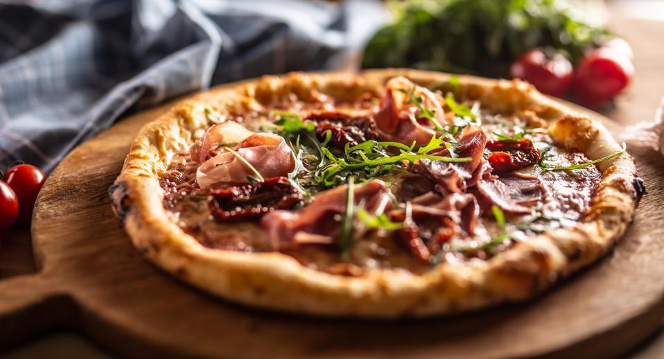 Freshly baked pizza with prosciutto, sun dried tomatoes and arugula leaves.
