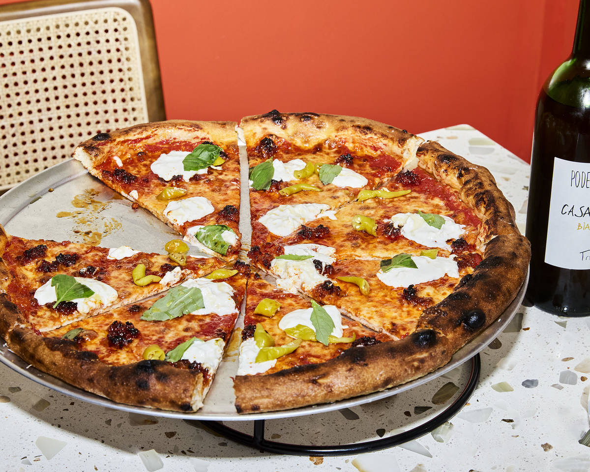 a delicious-looking pizza cut into slices, presented on a raised pizza platter, next to a bottle of wine