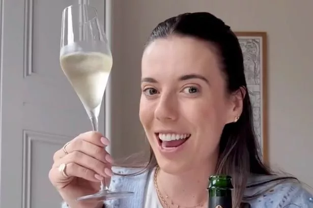 A picture of wine expert Lucy Hitchcock wearing a pale blue cardigan and toasting with a Champagne flute