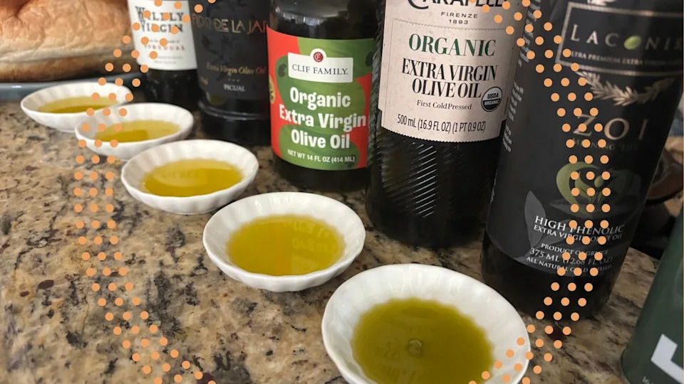 Five small dishes of olive oil sit on a table next to five bottles of olive oil.