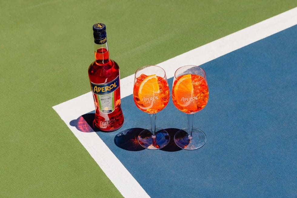 Aperol bottles and cocktails placed on a tennis court.
