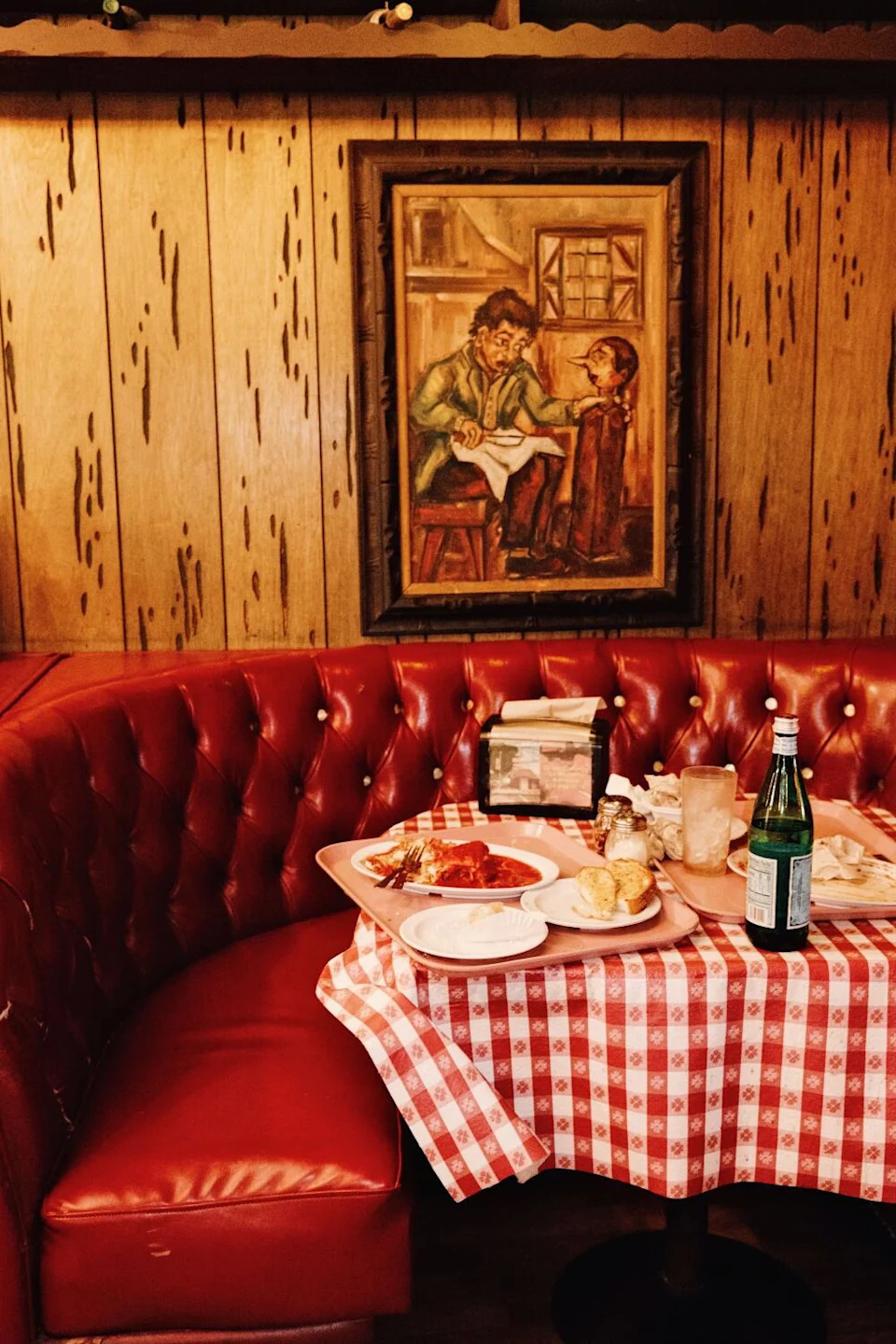 A painting of Pinocchio hanging over a red leather booth and a table of a finished meal