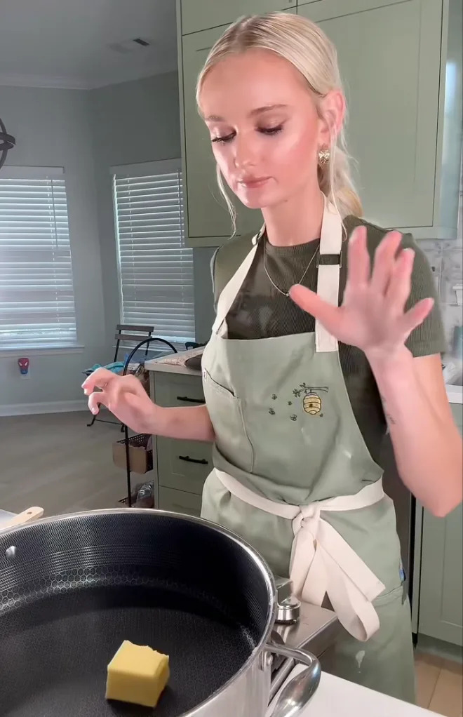 Person in a kitchen wearing an apron, preparing to cook with butter in a pan