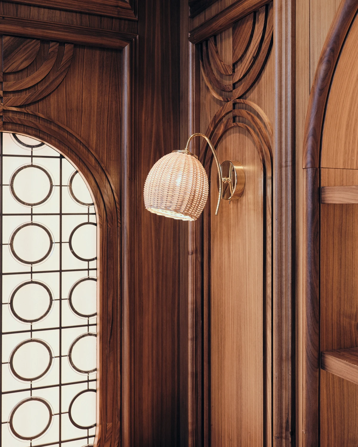 A modern rattan sconce adds a warm, natural glow to the wood-paneled walls at W Rome