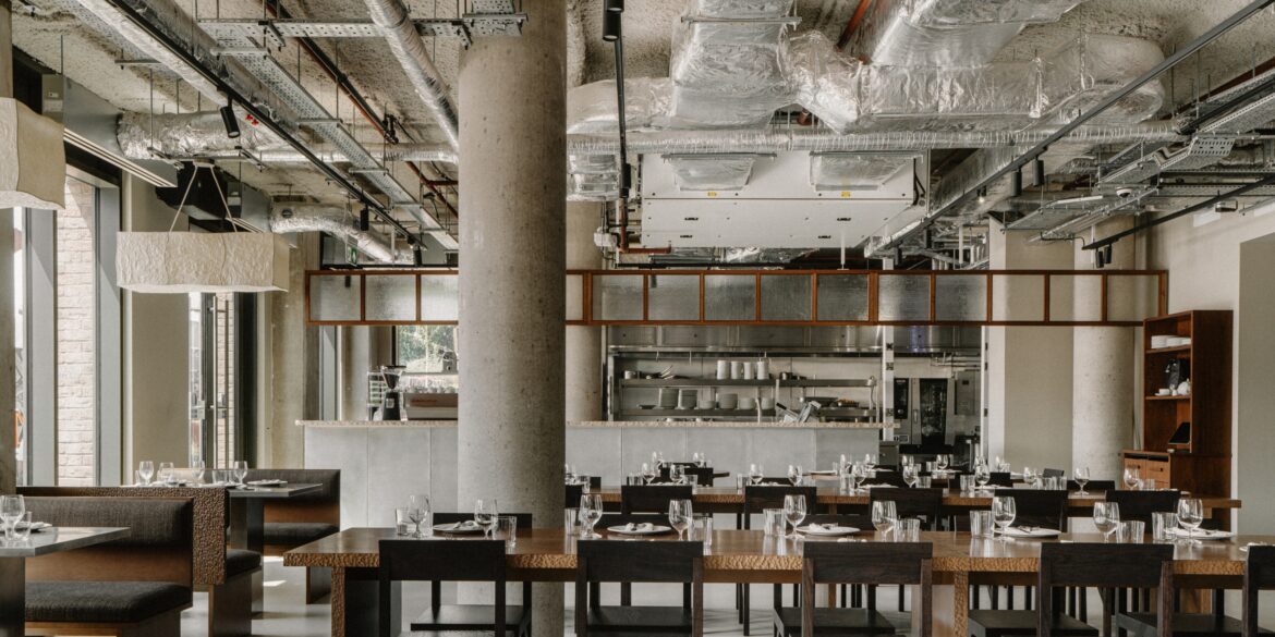 Canal Is the New Westbourne Park Eatery Pairing Brutalism and Warmth A brutalist restaurant with exposed cement walls, silver ventilation pipes, wooden furniture, and chrome-clad decor is ready for lunch service and brought to life by light.