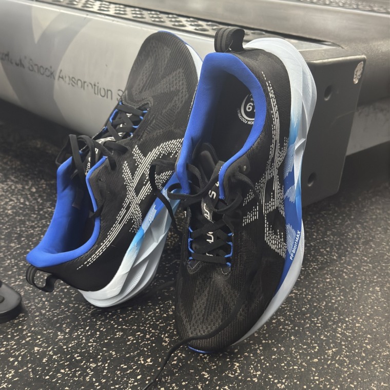 A close up shot of the Asics Novablast 5 in the blue and black version, leaning against the side of a treadmill.