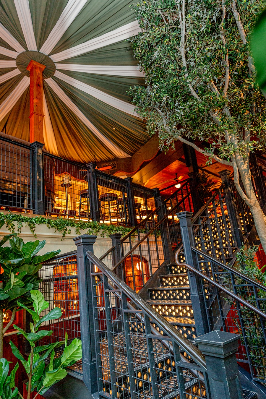 A two-story restaurant features lots of greenery and a green-and-white-striped canopy.
