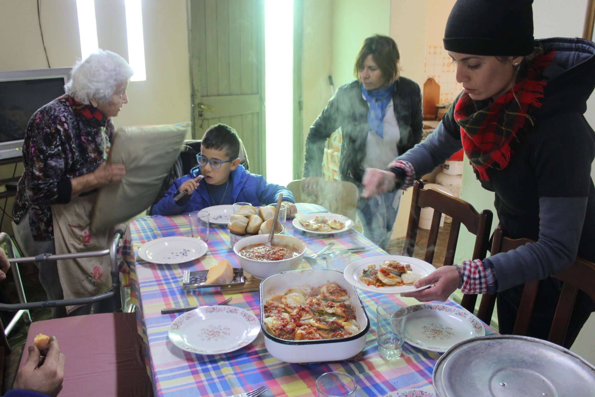 A family prepare to sit around a table full of dishes, including a sauce-covered baked dish unleashing waves of steam.