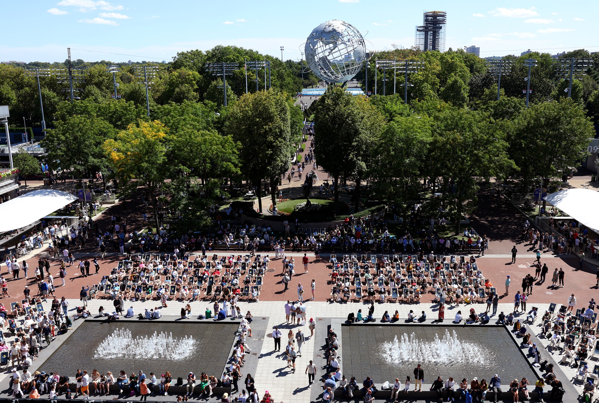 Crowds of people at a park with two fountains and a big sphere in the background