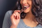 Cropped image of attractive girl eating chocolate and smiling, against dark background.