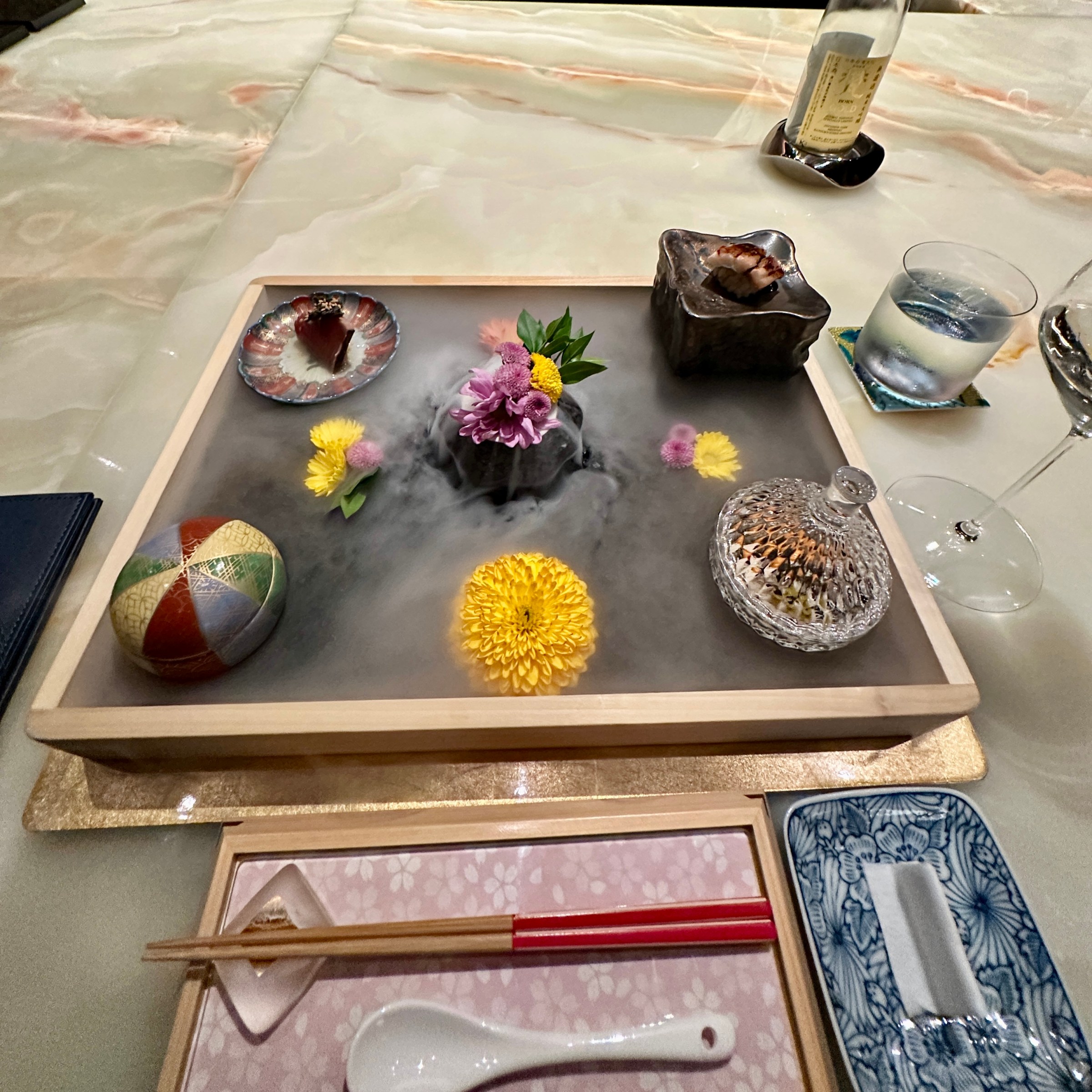 A tray of omakase dishes with liquid nitrogen flowing from a vase.