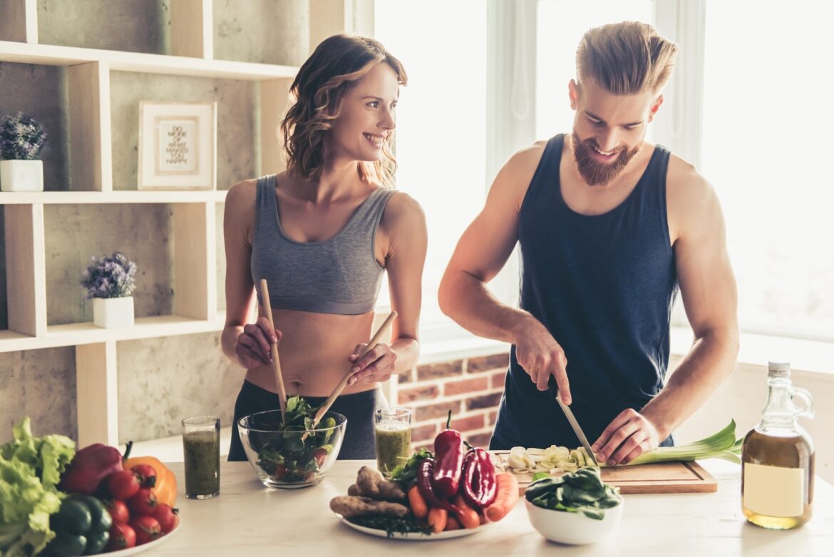 young sports people are talking and smiling while cooking healthy food in kitchen at home