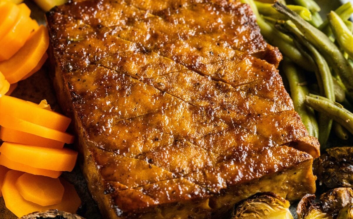 Photo shows a vegan tofu roast surrounded by roasted vegetables
