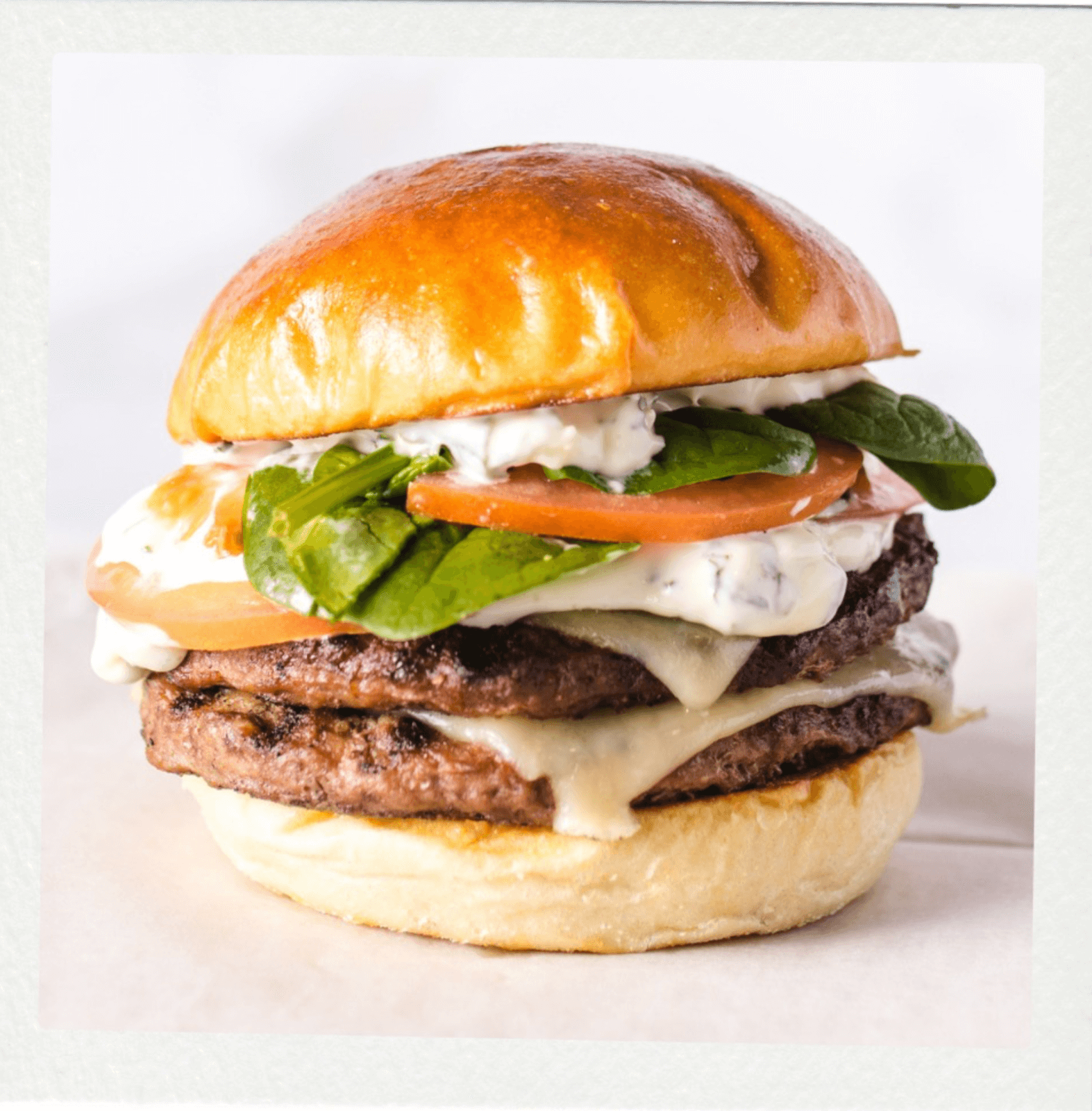A double cheeseburger with spinach, tomato, white sauce, and melted cheese on a shiny brioche bun—a must-try at new restaurants redefining dining concepts in Birmingham.