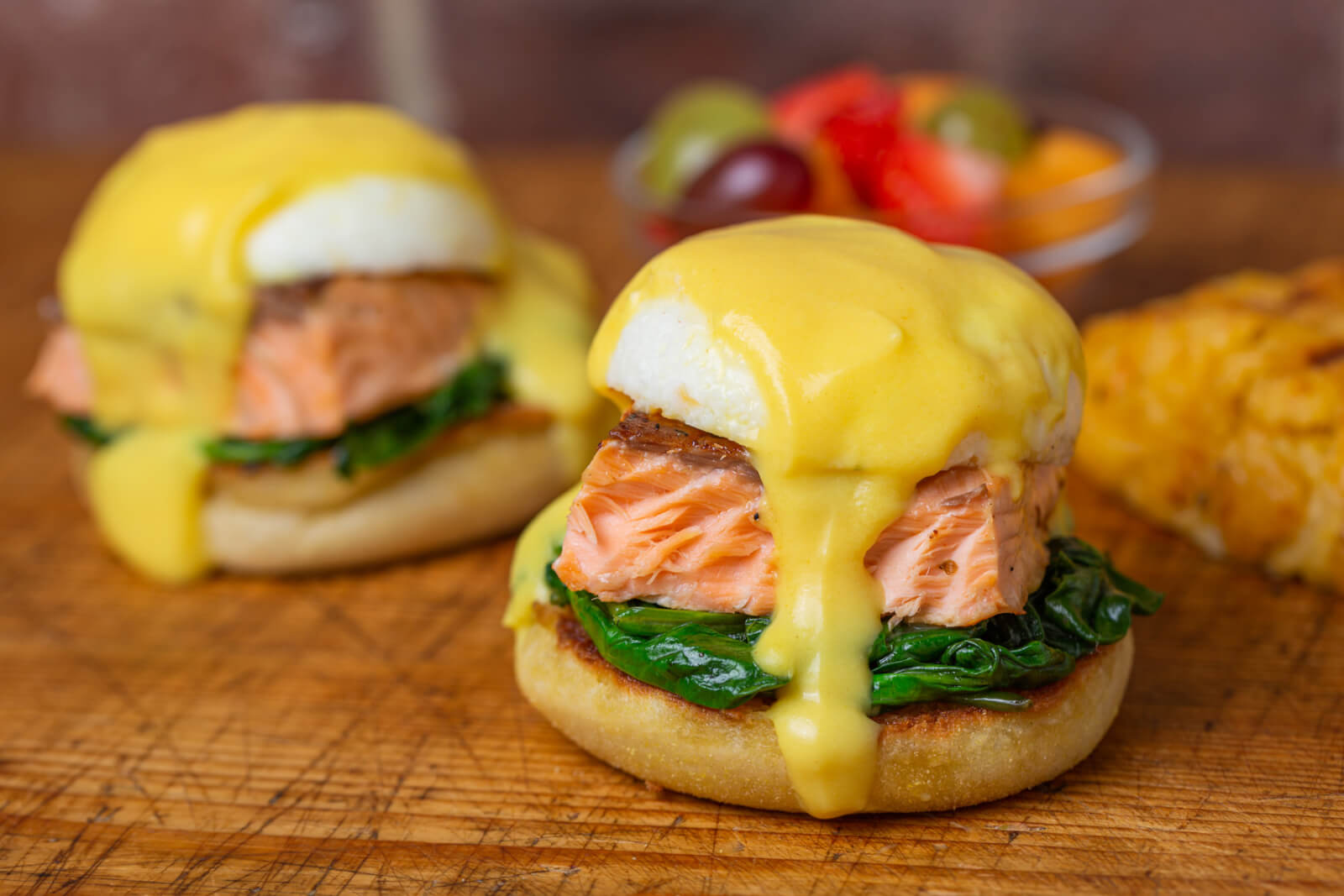 Two English muffins topped with sautéed spinach, salmon, poached eggs, and hollandaise sauce, with a side of fruit and potato casserole—perfect for dining at top Birmingham restaurants or discovering new restaurants in the city.